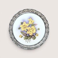 Vintage round porcelain tray featuring yellow hand-painted flowers in the center and a decorative pierced metal rim.