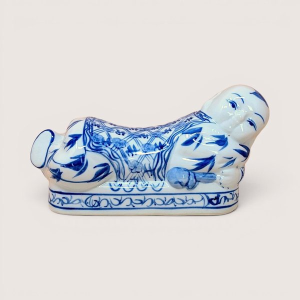 Blue and white vintage Chinese porcelain opium pillow shaped like a reclining boy against a plain background.