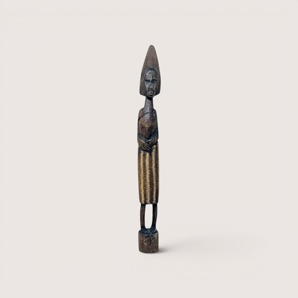Vintage tall and slender hand-carved African wooden standing figurine with geometric skirt patterns on a small circular base.