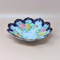 Scalloped porcelain bowl with a deep cobalt blue rim and intricate gold filigree. The interior features hand-painted pink and yellow floral bouquets with delicate green vines on a white ground.