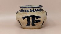 Hand-thrown pottery bowl with a globular shape and a sandy, textured tan glaze. Featuring bold, gestural cobalt blue brushstrokes including a large "PI" or "TF" symbol and a saw-tooth rim pattern.