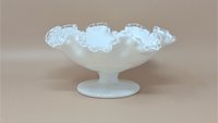 Fenton milk glass compote with a pedestal base and wide, ruffled rim. Features an opaque white body with a clear glass "Silver Crest" edge, set against a neutral background.