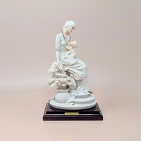 Giuseppe Armani "Maternal" porcelain figurine of a mother cradling an infant, seated beside a flowering tree. Set on a dark wood square pedestal base with a gold nameplate. Matte white and cream finish.