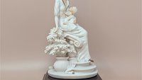 Giuseppe Armani "Maternal" porcelain figurine of a mother cradling an infant, seated beside a flowering tree. Set on a dark wood square pedestal base with a gold nameplate. Matte white and cream finish.