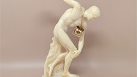 12-inch tall cream-colored bonded alabaster statue of the Discobolus (Discus Thrower). Features detailed muscle definition and a smooth, matte finish. Original "Hermes Greece" tag attached.