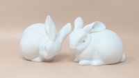 Pair of vintage Dept. 56 white porcelain bunnies in resting poses. Features a soft matte finish with realistic ear and fur detailing.