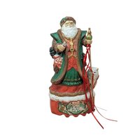 A hand-painted ceramic Old World Santa figurine on a musical base. He wears a green and red robe, holding a staff with red ribbons and a nutcracker. A white bear cub sits at his foot. The red base reads "Merry Ole Soul." The style is glossy and traditional against a plain beige background.