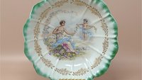Antique Dresden porcelain bowl with a scalloped edge and green ombré rim. Center features a classical scene of a woman and a cherub with floral garlands. Gold filigree accents. 9.25 inches wide.