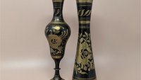 Pair of tall vintage brass vases with a black matte finish. Hand-etched floral designs reveal the golden brass beneath. One is a sleek bud vase; the other features a scalloped rim and a pedestal base. 11.75 inches tall.