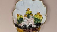 Scalloped Capodimonte porcelain trinket dish with a high-relief embossed scene of two children in a garden. Hand-painted in earthy tones with a gold gilt rim. 5.5 inches wide.