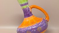 Hand-painted Spanish ceramic pitcher with a unique tilted, globular body. Features vibrant bands of purple, orange, and lime green with white raised "dot" slip-trailing and yellow floral motifs. 9.25 inches tall.