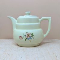 Hall China "Rambling Rose" cream ceramic coffee pot and lid. Features a tiered Art Deco body, an angular handle, and a delicate pink and blue floral spray. 7.75 inches tall.