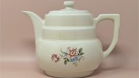 Hall China "Rambling Rose" cream ceramic coffee pot and lid. Features a tiered Art Deco body, an angular handle, and a delicate pink and blue floral spray. 7.75 inches tall.