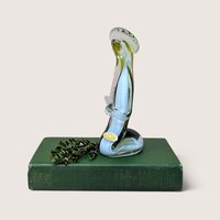 A vertical art glass sculpture of a person in a prayerful pose. A vibrant green inner layer is visible through the thick clear glass exterior, which curves into a stable, weighted base.