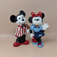 Set of two vintage 9-inch hand-painted Disney figurines. Dapper Mickey in a red-and-white striped jacket holding a brown hat. Minnie in a blue dress and red bow waving. Ceramic style.