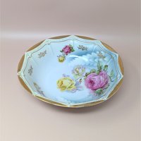 Scalloped octagonal porcelain bowl. Pale blue ombre interior with large pink and yellow roses. Wide rim features heavy gold gilt with a delicate beaded relief texture.