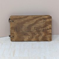 A small, rectangular autograph book with a natural wood grain cover. The words "Autograph Book" are hand-carved into the wood. Two metal rings bind the pages on the left. Rustic, weathered texture with a warm honey-oak finish.