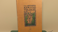 Antique book with a golden-yellow textured cloth cover. Features an Art Nouveau illustration of a woman with a hawk and a castle. Titled "The Young Folks Treasury" in stylized black font. Aged, tactile fabric finish.