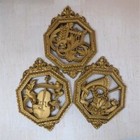 Set of three octagonal gold-toned wall plaques. Each features a different relief-style musical instrument: a lyre, a horn, and a violin. Ornate open-work frames with a metallic gilt finish.