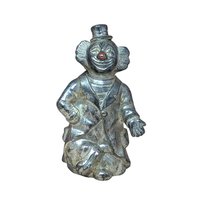 A vertical silver-toned metal bank shaped like a circus clown in a top hat and suit. Features an aged metallic patina with a small red detail on the nose. Sculptural, heavy-duty texture with a slot on the reverse.