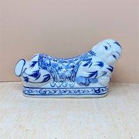 A horizontal porcelain headrest shaped like a reclining child. Featuring a crisp white ground with traditional cobalt blue floral and scroll patterns. Glossy vitrified texture with hand-painted facial details.