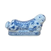 A horizontal porcelain headrest shaped like a reclining child. Featuring a crisp white ground with traditional cobalt blue floral and scroll patterns. Glossy vitrified texture with hand-painted facial details.
