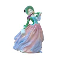 A vertical porcelain figurine of a woman in a wind-swept gown. She wears a vibrant green bodice, a wide-brimmed hat, and a voluminous skirt in blended shades of pink, peach, and lavender. Glossy, fine-bone china texture.