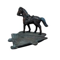 A vertical cast metal ashtray featuring a saddled horse figurine standing on a triangular base. The metal has a dark bronze patina with heavy green verdigris oxidation throughout. Sturdy, industrial texture with period-correct relief details.