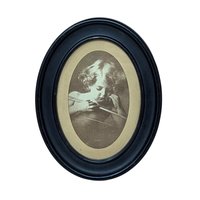 An oval vintage sepia-toned print titled "Cupid Asleep" by M.B. Parkinson. It depicts a young child with curls leaning over a bow. The print is housed in a thick, matte black wooden oval frame. 8.5 by 6.75 inches.A vintage sepia-toned oval print of M.B. Parkinson's "Cupid Asleep" featuring a young child with wings holding a bow. Housed in a black oval wooden frame with visible surface scrapes and aging.