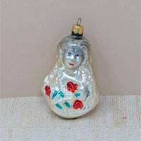 A vintage mercury glass ornament featuring a Victorian-style girl with long, flowing hair holding a bouquet of red roses with green leaves. The glass has a warm, milky-white luster with hand-painted facial details.