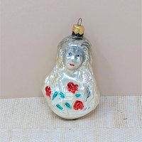 A vintage mercury glass ornament featuring a Victorian-style girl with long, flowing hair holding a bouquet of red roses with green leaves. The glass has a warm, milky-white luster with hand-painted facial details.