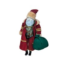 An 18-inch Santa Claus figure standing on a white base. He wears a deep red velvet robe with gold braided trim and a fur-trimmed hood, holding a green velvet toy sack and featuring a detailed ceramic face.