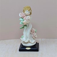 A finely detailed porcelain figurine of a young girl in a flowing white dress holding a large bouquet of pink roses. She stands on a dark wooden base with a gold Florence Giuseppe Armani plaque.