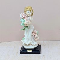A finely detailed porcelain figurine of a young girl in a flowing white dress holding a large bouquet of pink roses. She stands on a dark wooden base with a gold Florence Giuseppe Armani plaque.