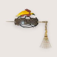 Carved wooden tribal hair slide featuring a yellow and brown bird of paradise motif, complete with a matching hair pin and attached fan-like dangle, isolated on a light neutral background.