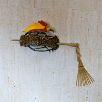 A hand-carved wooden hair slide featuring a red and yellow bird perched atop an ornate brown base with geometric carvings. A wooden pin with a dangling tassel secures it. 4 inches wide.