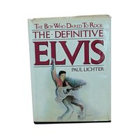 A large hardcover book titled The Boy Who Dared To Rock: The Definitive Elvis. The white dust jacket features an illustration of Elvis Presley in a pink jacket with a guitar. The jacket shows visible edge wear and small tears.