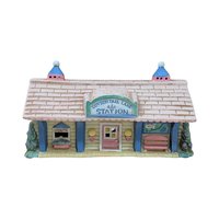 A vintage ceramic lighted house titled Cottontail Lane Station. It features a pink shingled roof with blue cupolas and a yellow clapboard exterior. The front includes a ticket window, a pink door, and a tiny bench under a "You Are Here" map.