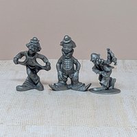 A trio of vintage silver-toned pewter clown figurines. One is in a deep curtsy, another is mid-stride in a classic circus pose, and the third is a dapper clown with a tall hat and buttons. Each figure has a matte metallic finish with fine sculptural details.