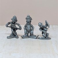 A trio of vintage silver-toned pewter clown figurines. One is in a deep curtsy, another is mid-stride in a classic circus pose, and the third is a dapper clown with a tall hat and buttons. Each figure has a matte metallic finish with fine sculptural details.