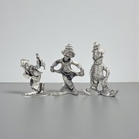 A set of three vintage silver-toned pewter clown figurines in different poses, including one bowing in a curtsy, one standing with hands in pockets, and one in a playful walking stance.