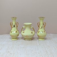 A collection of four vintage yellow ceramic vessels with bright gold accents. Includes a matching trio of Art Deco style vases with handles and gold leaf motifs, and a single rounded pitcher-style bud vase featuring a raised gold rose design.