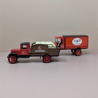 Two vintage red and brown die cast metal Anheuser Busch delivery truck banks. One is a flatbed carrying white yeast sacks, the other is an A and B Ice Cream panel truck.