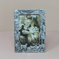 A vertical cast-metal picture frame with a weathered silver finish. Embossed hunters on horses and a pack of running hounds frame a portrait of a young girl with flowers.