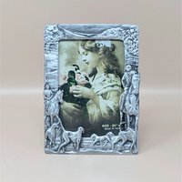 A vertical cast-metal picture frame with a weathered silver finish. Embossed hunters on horses and a pack of running hounds frame a portrait of a young girl with flowers.