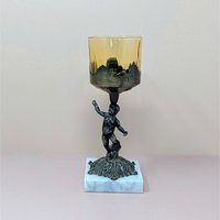 A 9-inch vintage candle holder featuring a dark cast metal cherub figure standing on a white marble square base, supporting a translucent amber glass cup.