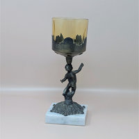 A 9-inch vintage candle holder featuring a dark cast metal cherub figure standing on a white marble square base, supporting a translucent amber glass cup.
