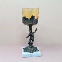 A 9-inch vintage candle holder featuring a dark cast metal cherub figure standing on a white marble square base, supporting a translucent amber glass cup.