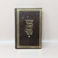 A 1976 hardcover edition of Uncle Tom's Cabin by Harriet Beecher Stowe with a dark brown textured cover and gold gilt lettering and borders