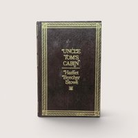 A 1976 hardcover edition of Uncle Tom's Cabin by Harriet Beecher Stowe with a dark brown textured cover and gold gilt lettering and borders